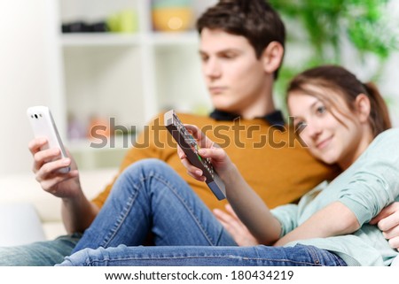 beautiful woman watching tv while her lover is watching a screen of cell