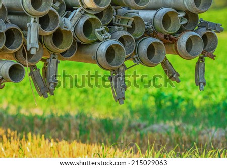 Metallic tubes being transported through the field, arranged and held right above the green grass