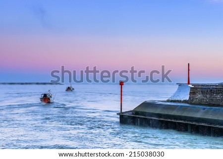 Two ships leaving the harbor and sailing across the sea  towards the colorful horizon line
