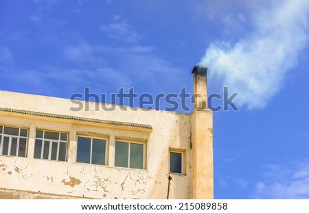 Upper floor of a building with ysmoke coming out of the chimney and clear blue sk