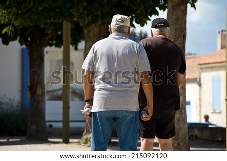 Two old men walking in the street, with one of them holding two metallic balls in his hands