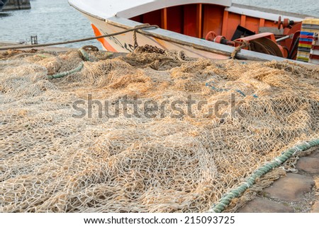 Huge white fishing net spread on the ground with a small boat on the second plan tied to the shore