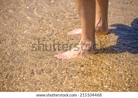 A pair of bare legs standing on the soft wet sand on the beach in the sun