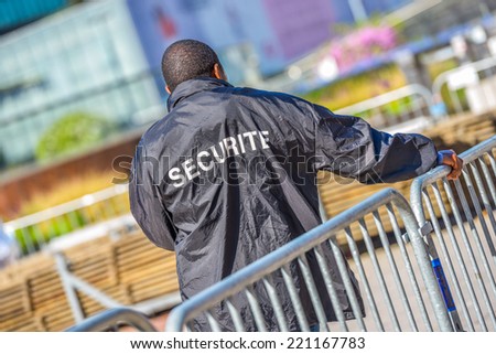 Security worker leaning over metallic fence and watching over the construction area