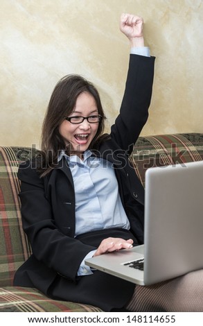 Woman in business suit on sofa cheering with laptop