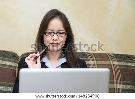 Woman in business suit on sofa in deep thought, with pen and laptop