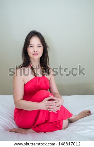 Woman in red dress posing in bed sitting and hugging knees