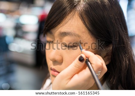Young Asian woman applying eye liner with a small brush