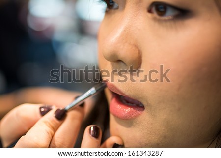 Young Asian woman applying lipstick and other cosmetics