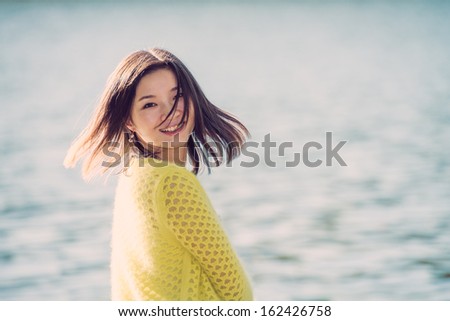 Portrait of young attractive woman sitting on a rock next to a river looking back with floating hair