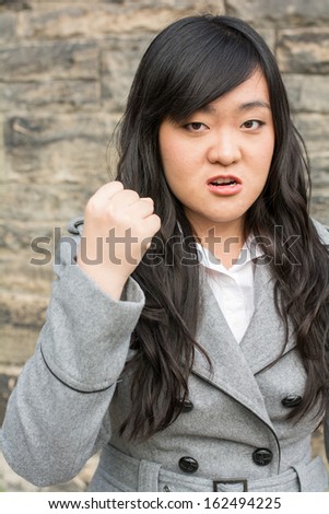Portrait of young aggressive woman in front of a stone wall looking angry and holding fist