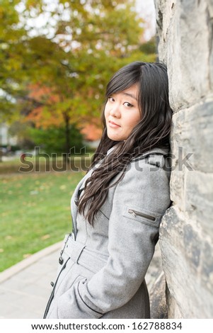 Portrait of young woman standing back against a stone wall looking innocent
