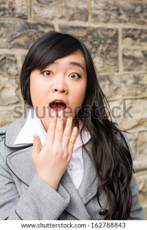 Portrait of attractive young woman looking surprised and trying to cover mouth