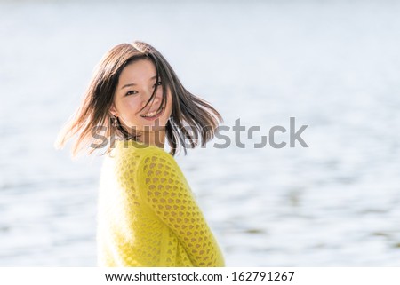 Portrait of young attractive woman sitting on a rock next to a river looking back with floating hair