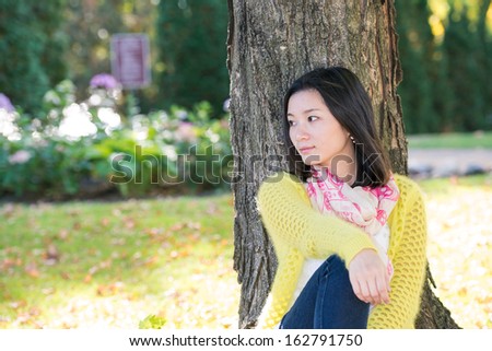 Portrait of happy looking woman sitting against a tree and looking to the side