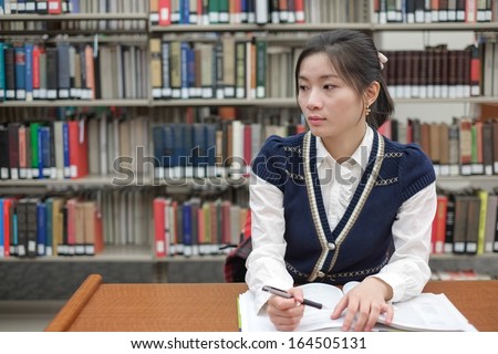 Portrait of young female student on sitting at a desk in front of a library shelf