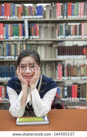 Portrait of young female student on sitting at a desk in front of a library shelf