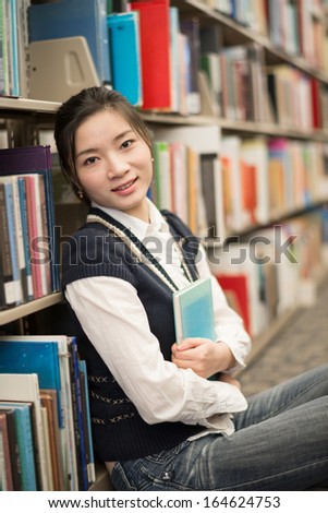 Cute young girl hugging a blue book while sitting in front of a bookshelf