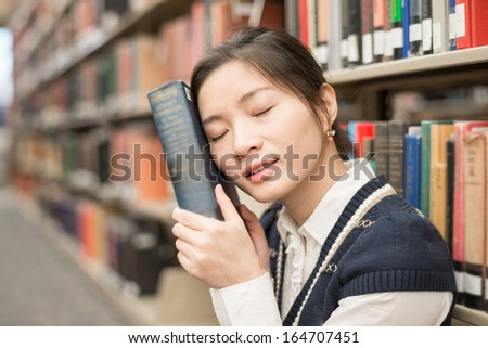Young girl sitting in front of a bookshelf resting head on a thick old book