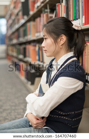Attractive young girl sitting on the floor in front of a bookshelf holding a thick old book