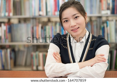 Young student resting on a wooden shelf in front of a bookshelf in library