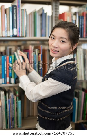 Portrait of young clever student standing in front of a bookshelf in library