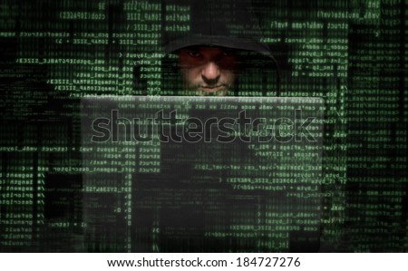 Silhouette of a hacker looking in camera with binary codes on monitor