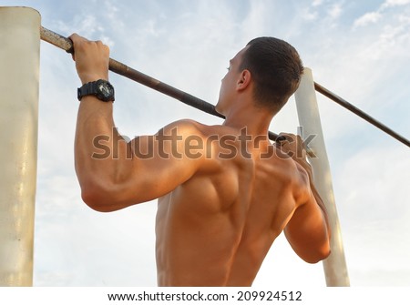 Closeup of strong  athlete doing pull-up on horizontal bar.Mans fitness with blue sky in the background and open space around him