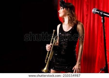 Woman on stage play on the trumpet.Red velvet curtain  on background