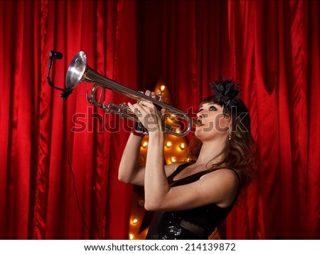 Woman on stage play on the trumpet.Red velvet curtain  on background