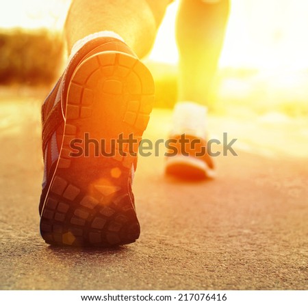 Athlete runner feet running on treadmill closeup on shoe.Mans fitness with the sun effect of fall autumn colors in the background