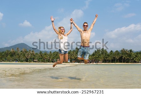 couple bounces cross-legged on the beach holding hands and lifting them up