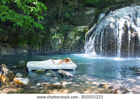 A hidden place. Sleeping woman in deep forest lies on airbed. Waterfall on back
