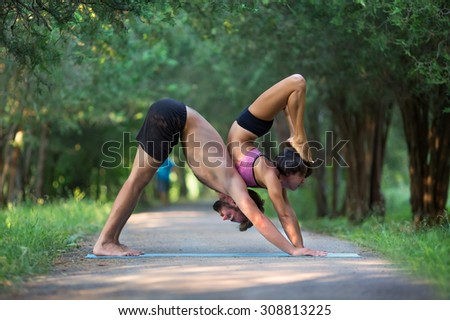 Acro yoga, two sporty people practice yoga in pair, couple doing stretching exercise in the garden