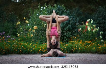 Acro yoga, two sporty people practice yoga in pair, couple doing stretching exercise in the garden.