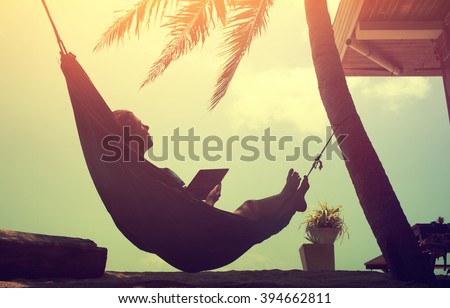 Woman an using a digital tablet computer while relaxing in a hammock