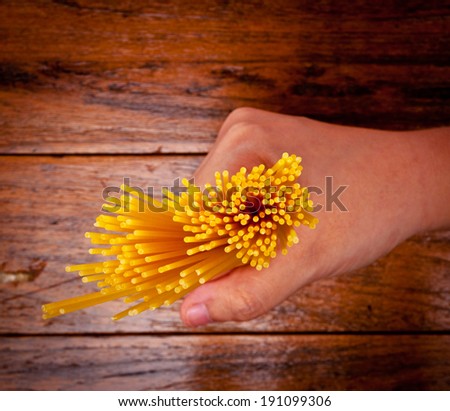 Human Hand Holding Fresh Spaghetti Pasta Italian Dish on Wood Table, Rustic Style.