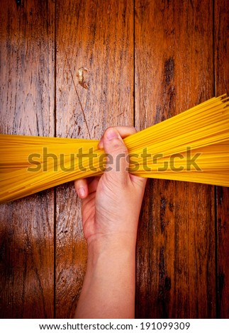 Human Hand Holding Fresh Spaghetti Pasta Italian Dish on Wood Table, Rustic Style.