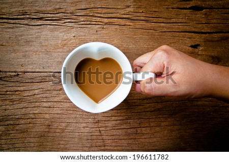 Hand Holding Drinking, Coffee Mug in Design of Heart Shape, Love and romantic idea on Wood Table Background, Rustic Style.