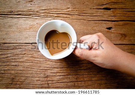 Hand Holding Drinking, Coffee Mug in Design of Heart Shape, Love and romantic idea on Wood Table Background, Rustic Style.