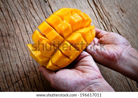Hand Holding Fresh Mango , Cut in Square Shape Concept of Food Art, Idea of Decorated Food, On Wood Table Background, Rustic Style.