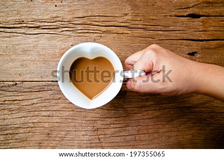 Hand Holding Drinking, Coffee Mug in Design of Heart Shape, Love and Romantic or Valentine\'s Concept and idea on Wood Table Background, Rustic Style.