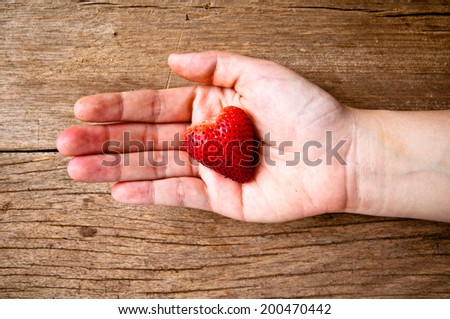 Hand Holding Fresh Strawberry in Heart Shape on Wood Table Background, Rustic Still Life Style. / Concept and idea of Food Decoration and Love Romantic.