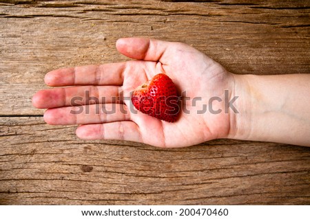 Hand Holding Fresh Strawberry in Heart Shape on Wood Table Background, Rustic Still Life Style. / Concept and idea of Food Decoration and Love Romantic.