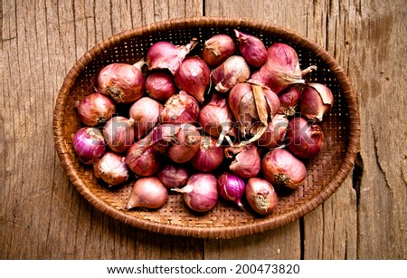 Group of String Fresh Red Onion Unpeeled with Woven Basket kitchenware harvest from farm garden on Wood Table Background, Rustic Still Life Style.