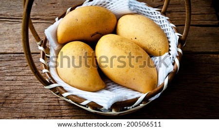 Fresh Yellow Ripe Mango Harvest in Woven Basket with Foam Package on Wood Table Background, Rustic Still Life Style.