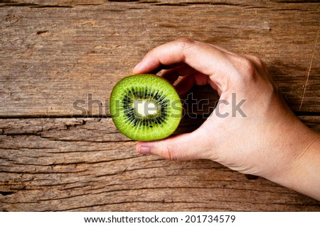 Hand Holding (Harvest,Show,Select,Pick,Choose) Fresh Group of Kiwi Fruits Sliced on Wood Table Background, Rustic Still Life Style.