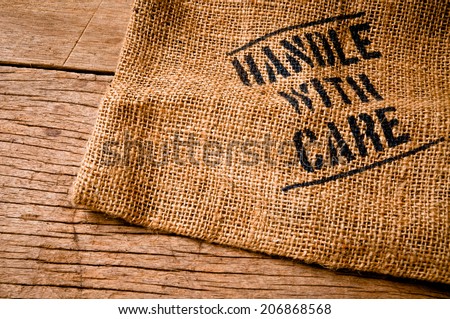 Vintage Burlap Bag with Handle with Care word text screen on Wood Table for Concept and Idea of Food, Art, Object, Kitchen Background and Textured, Country Rustic Still Life Style.