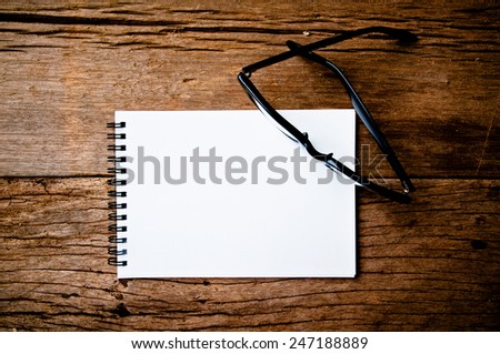 Clear Eyeglasses Glasses with Black Frame Fashion and Blank Note Book  / Vintage Style on Wood Desk Background, Rustic Still Life Style. Concept and Idea for Art and Education, Write Your Text Here.
