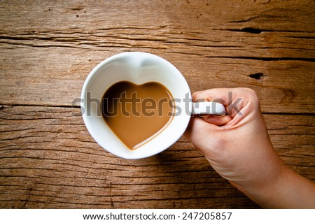 Hand Holding Drinking Coffee Mug in Design of Heart Shape, Love and Romantic or Valentine\'s Day Concept and idea of Love Sweet Sharing on Wood Table Background, Rustic Still life Style.
